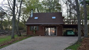 Une cabane en rondins avec une allée en briques, un abri-voiture couvert et une cheminée.