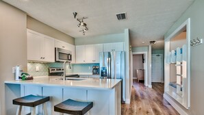 Cocina moderna con armarios blancos, una isla central con taburetes, un microondas y un refrigerador.