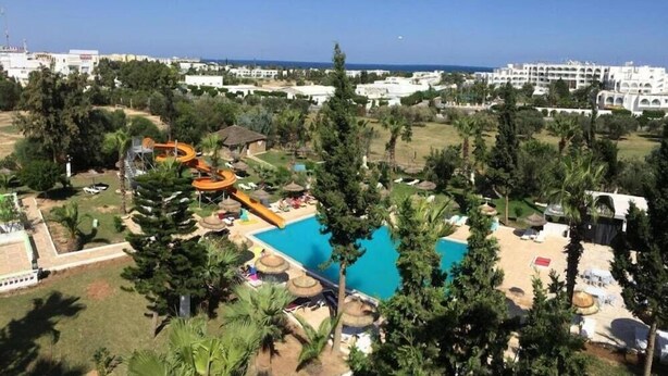 Um resort com piscina, palmeiras e vista para o mar.