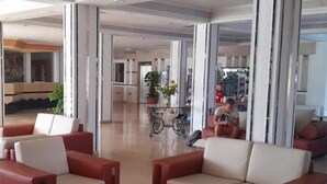 Um lobby de hotel moderno com sofás vermelhos e bege, uma mesa de centro de vidro e vista para a área da cozinha.