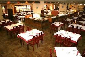 Ein Restaurant mit mehreren Tischen und Stühlen, einer Theke mit Registrierkasse und einem Küchenbereich im Hintergrund.