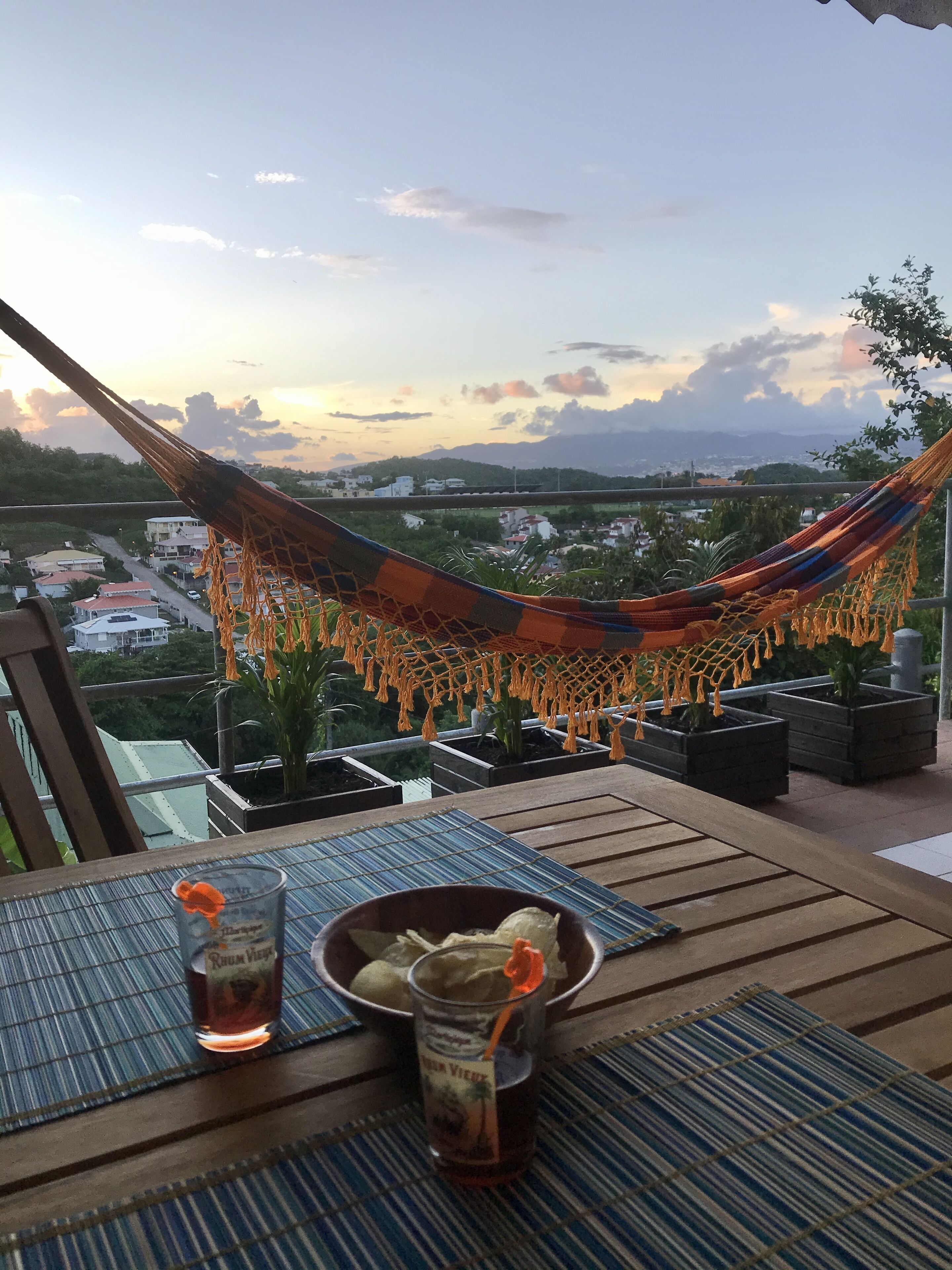 A hammock on a balcony overlooking a cityscape at sunset.