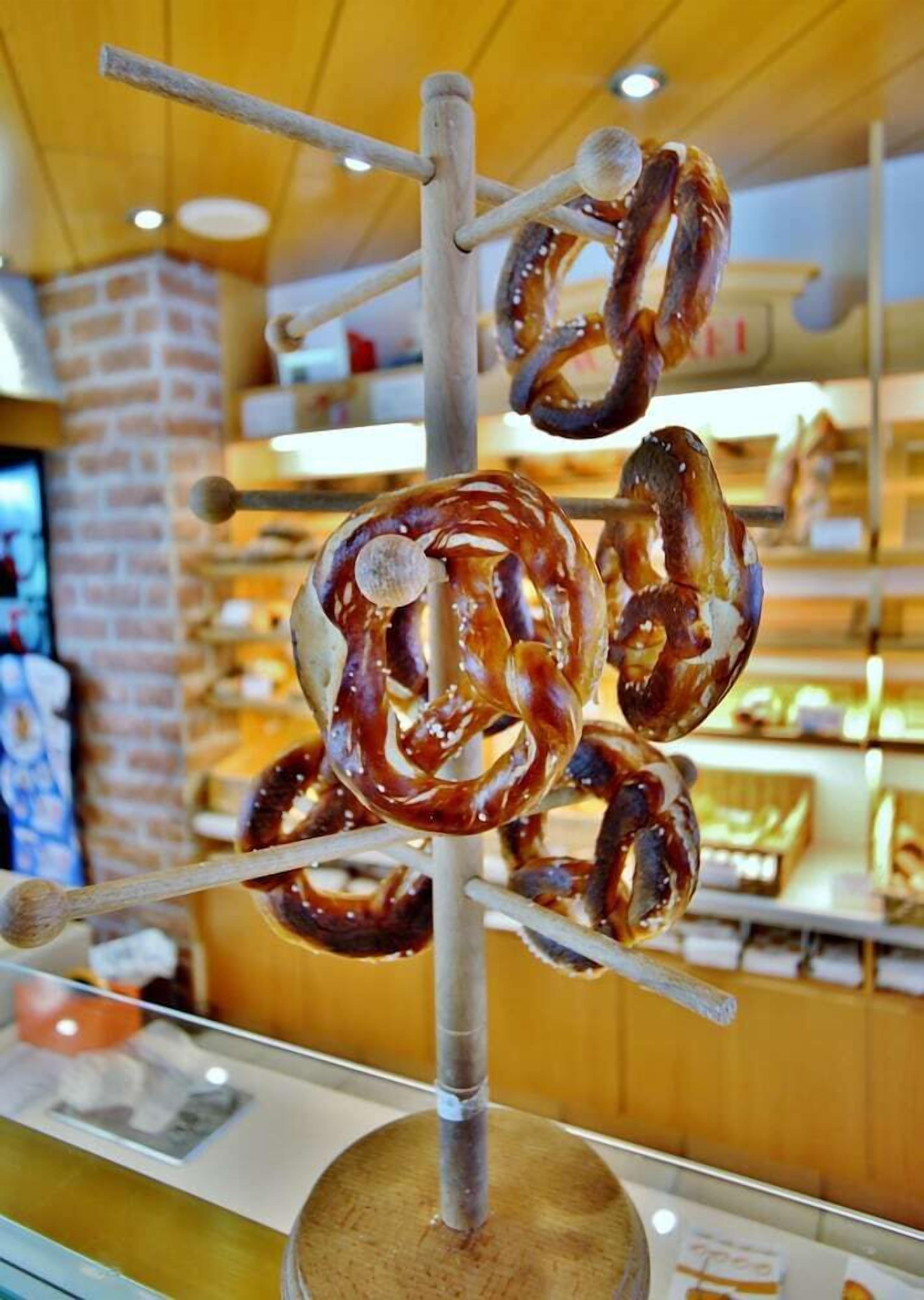 Des bretzels sont exposés, suspendus à une étagère en métal dans une boulangerie.