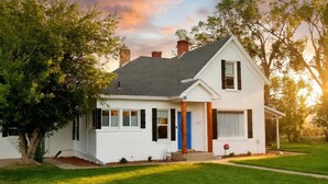 A single-story house with a white exterior, a blue door, and a chimney. - Restored 1920s Corner Cottage – Bryce Gateway Retreat (Panguitch)