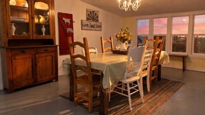 A dining area with a wooden table, chairs, a chandelier, and a view of the sunset through large windows. - Restored 1920s Corner Cottage – Bryce Gateway Retreat (Panguitch)