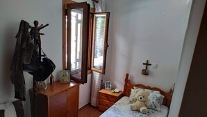 A bedroom with a wooden bed, a bedside table with a teddy bear, a dresser with a mirror, and a window with curtains.