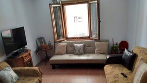 A living room with a sofa, chairs, a TV, and a window with curtains.