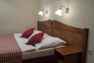 Una cama bien hecha con una colcha a cuadros y dos almohadas rojas, un cabecero de madera y dos lámparas fijadas a la pared.