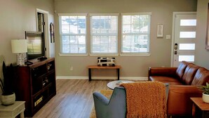 Un salon avec un canap é en cuir marron, un fauteuil bleu, une table basse en bois et un téléviseur posé sur un meuble en bois.