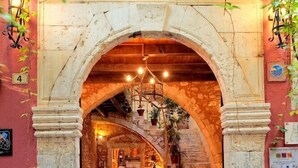 An arched entrance to a building with a stone facade, a wooden door, and a red carpet leading inside. - Veneto Boutique Hotel (Rethymno)