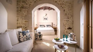 A bedroom with a stone wall, a bed, a nightstand, a coffee table, and a sofa. - Veneto Boutique Hotel (Rethymno)
