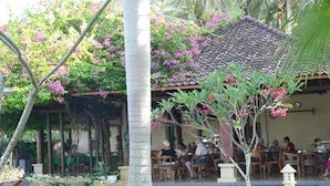 A restaurant with outdoor seating, a palm tree, and a tiled roof. - Puri Saron Senggigi Beach Hotel (Senggigi)