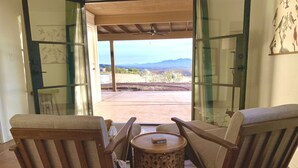 Una habitación con dos sillas de madera y una pequeña mesa redonda, una puerta de cristal que da a un patio exterior con vistas a montañas.