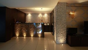 A modern lobby with a stone-textured reception desk, a chandelier, and a flat-screen TV on a cabinet. - Ocean View (Pangaio)