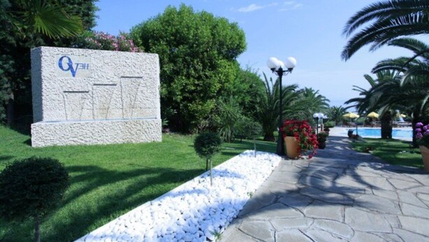 A stone sign with a logo, surrounded by a well-maintained garden with white pebbles, a pathway, and palm trees. - Ocean View (Pangaio)