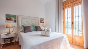 A neatly arranged bedroom with a large bed, a nightstand with a lamp, and a window with a view. - Casa Mari de Almogía by Ruralidays (Málaga)