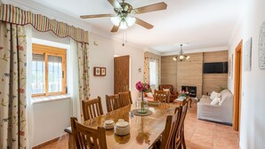 A dining area with a wooden table and chairs, a ceiling fan, and a TV mounted on the wall. - Casa Mari de Almogía by Ruralidays (Málaga)