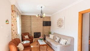 A living room with a fireplace, leather armchair, sofa, and a chandelier. - Casa Mari de Almogía by Ruralidays (Málaga)