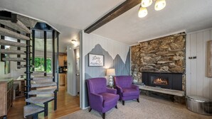Een gezellige woonkamer met een stenen openhaard, een krabpaal en twee paarse fauteuils.