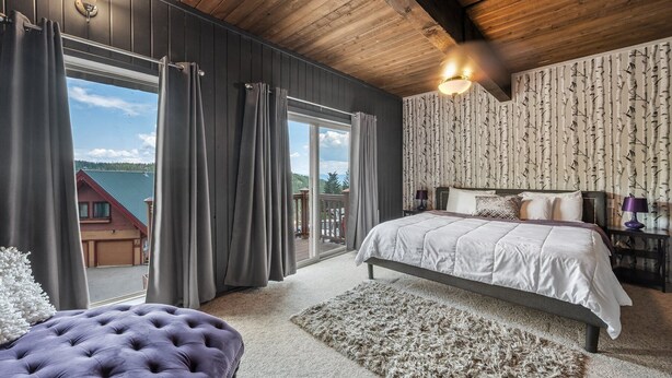 Een slaapkamer met een groot bed, een gestuufd poefje, uitzicht door een schuifdeur en een houten plafond.