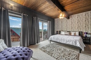 A bedroom with a large bed, a tufted ottoman, a view through a sliding door, and a wooden ceiling. - Great location! Historic Schwietzer condo. 1/2 mile to lifts. Mountain views. (Sandpoint)