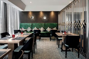 Un comedor de hotel moderno con un sofá tapizado en verde, sillas negras y una alfombra estampada.