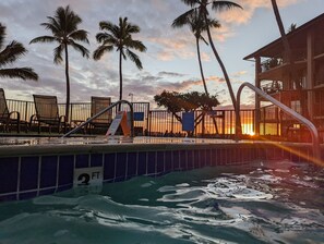 A swimming pool with palm trees and a sunset in the background.