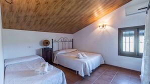 A bedroom with two beds, a wooden ceiling, a wall-mounted air conditioner, and a window with blinds. - Casa Rural Huertas del Rio Archidona by Ruralidays (Málaga)