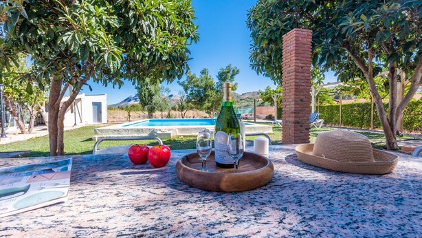 A table with a bottle of wine, two red apples, and a straw hat. - Casa Rural Huertas del Rio Archidona by Ruralidays (Málaga)