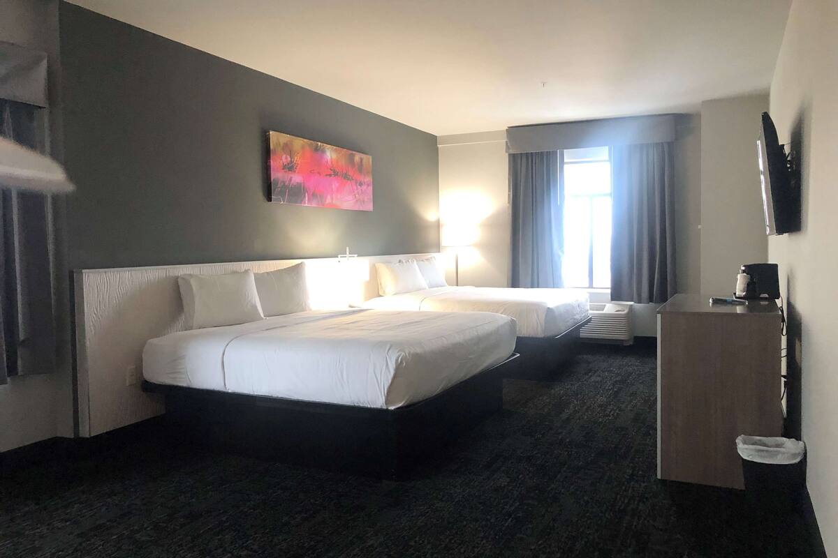 A hotel room with two beds, a desk, a chair, a TV, and a window with curtains.