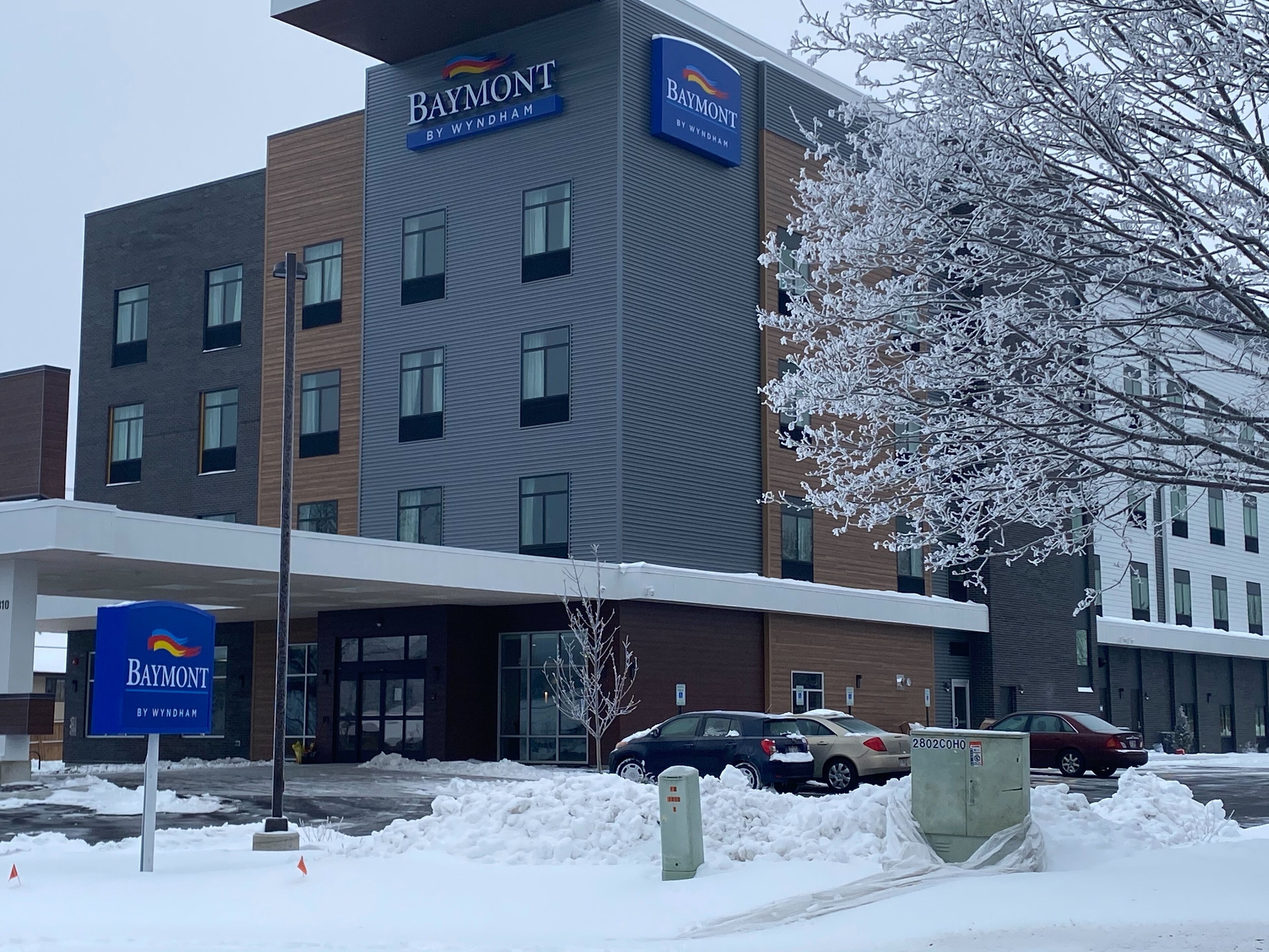 Un hôtel Baymont by Wyndham doté d’une façade moderne, de nombreuses fenêtres et d’un parking enneigé.