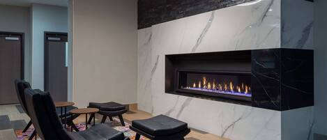 A modern lounge area with a fireplace, black leather seating, and a patterned rug.