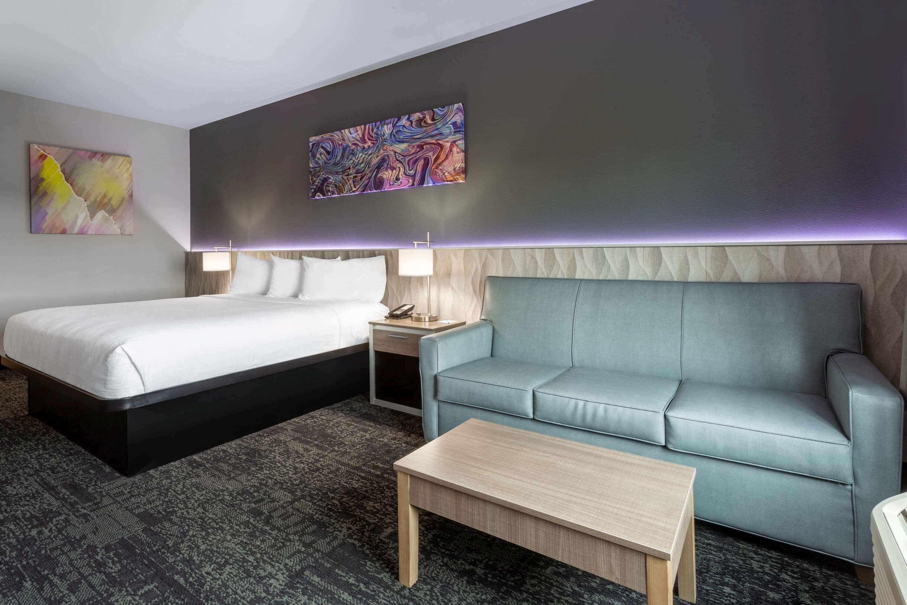 A hotel room with a bed, a sofa, a nightstand, and a table.