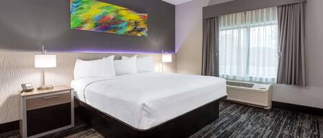 Une chambre d’hôtel avec un grand lit, une table de chevet avec une lampe, un climatiseur fixé au mur et une fenêtre avec des rideaux.