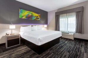 A hotel room with a large bed, a bedside table with a lamp, a wall-mounted air conditioner, and a window with curtains. - Baymont Inn & Suites by Wyndham Madison (Madison)