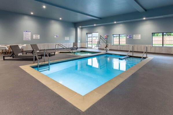 An indoor swimming pool with clear water, lounge chairs, and safety signs. - Baymont Inn & Suites by Wyndham Madison (Madison)