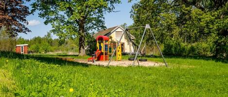 A playground with swings and slides, surrounded by lush greenery and trees.