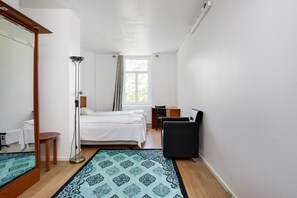A bedroom with two beds, a desk, a chair, a floor lamp, and a window with curtains.