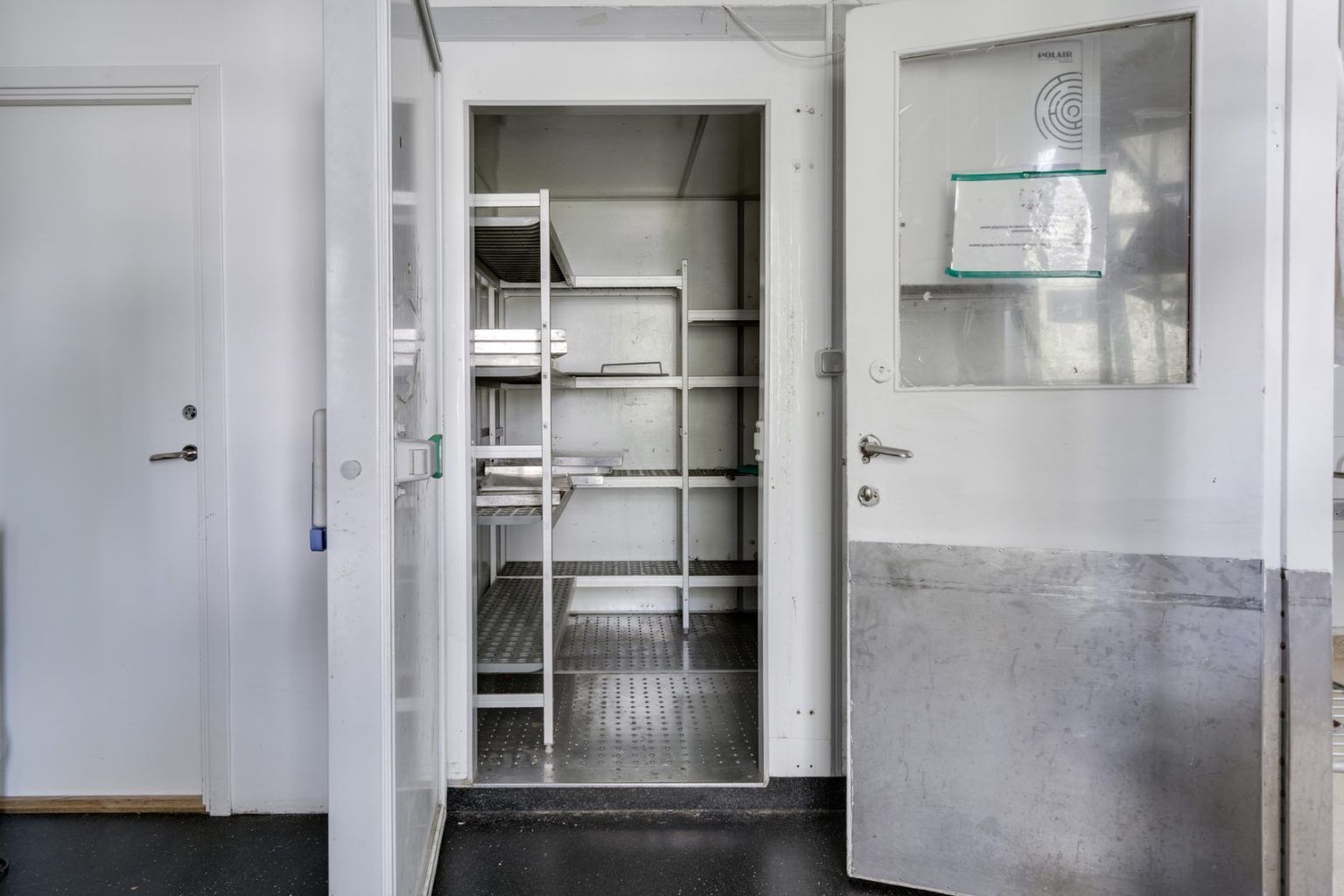 Une pièce propre, de style industriel, avec des étagères en métal et une porte dotée d’un panneau en verre dépoli.