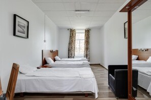 A hotel room with three single beds, a wooden headboard, a small round table, and a black sofa.