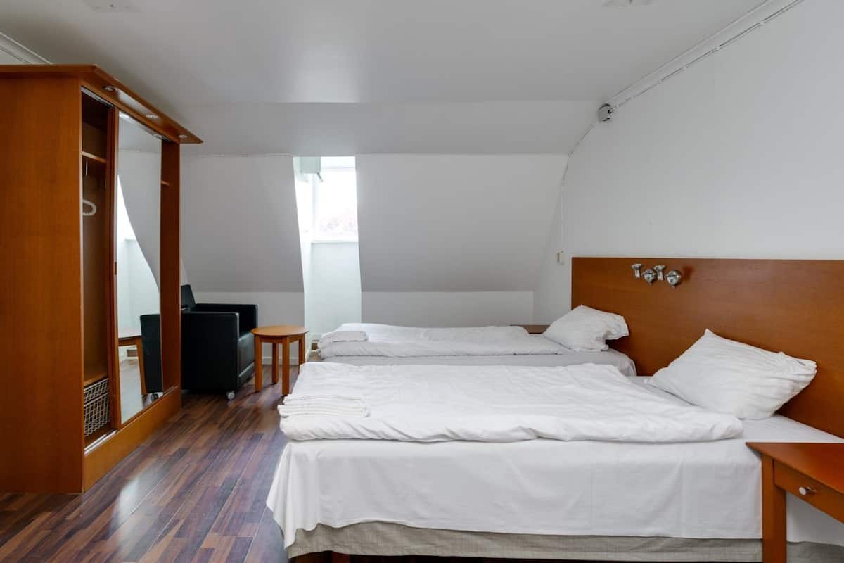 Un dormitorio con dos camas, un armario de madera, un radiador y una mesita.