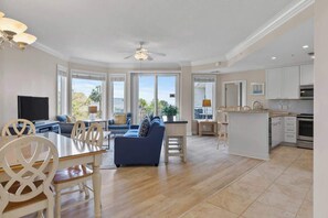 A spacious living area with a sofa, dining table, and chairs, a kitchen with cabinets and appliances, and large windows offering a view.