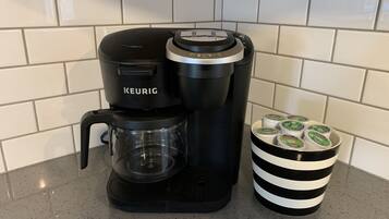 Une machine à café Keurig dotée d’une verseuse en verre et d’une tasse à rayures noires et blanches, remplie de capsules Keurig.
