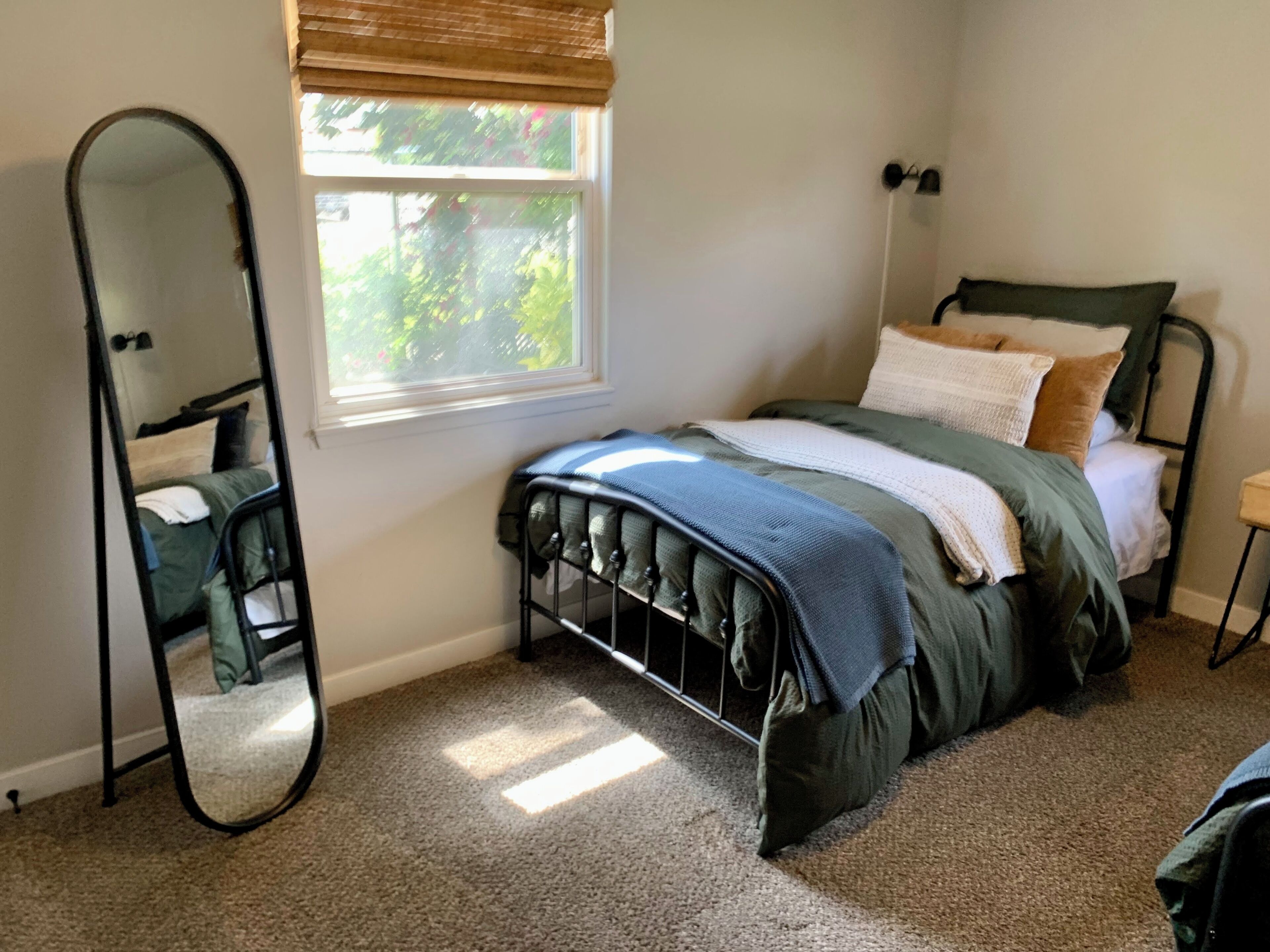 Une chambre à coucher avec un lit, un miroir, une fenêtre et une table de chevet.