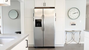 A modern kitchen with a stainless steel refrigerator, white cabinetry, a round wall clock, and a small table with a unique metal base. - Peaceful park-like Getaway (Richland)