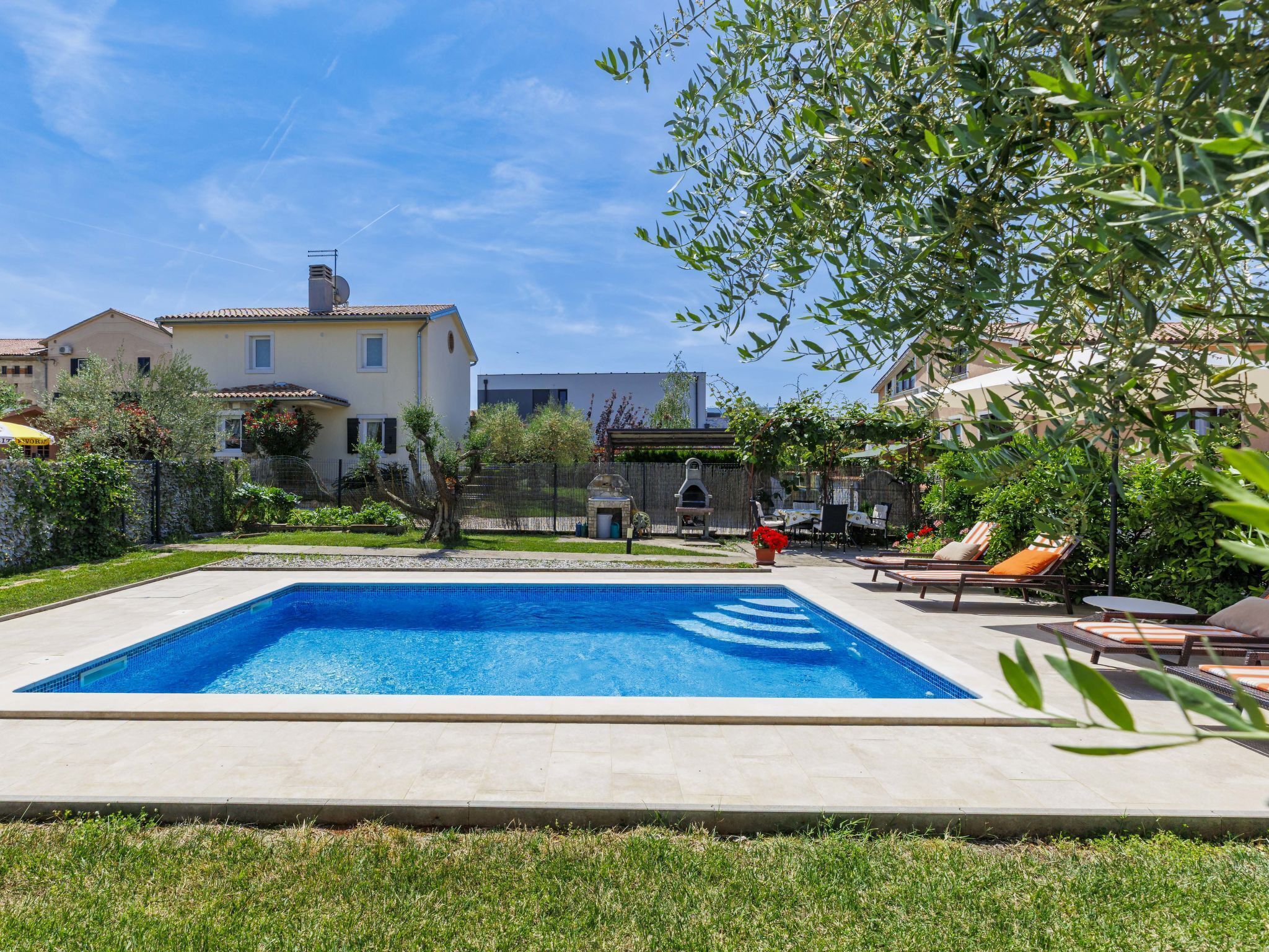 A swimming pool with a tiled deck, surrounded by a grassy lawn and a fence.