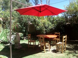 Un espace extérieur aménagé en terrasse, avec un parasol rouge, des chaises en bois et une table.