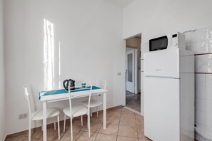 Une petite cuisine équipée d’un réfrigérateur blanc, d’un four à micro-ondes et d’une machine à café posés sur le plan de travail.