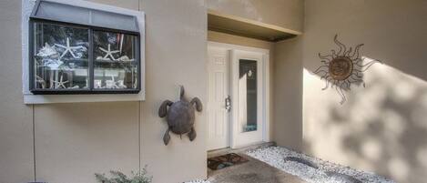 Exterior de una casa con una escultura de tortuga, una ventana decorada con estrellas de mar y un adorno de pared con forma de sol.