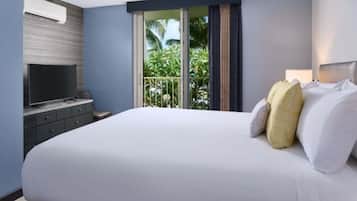 Una habitación de hotel con una cama grande, un televisor de pantalla plana sobre un aparador y vistas a palmeras a través de la ventana.